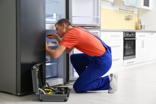 Male-Technician-With-Screwdriver-Repairing-Refrigerator-in-Kitchen-1024x680